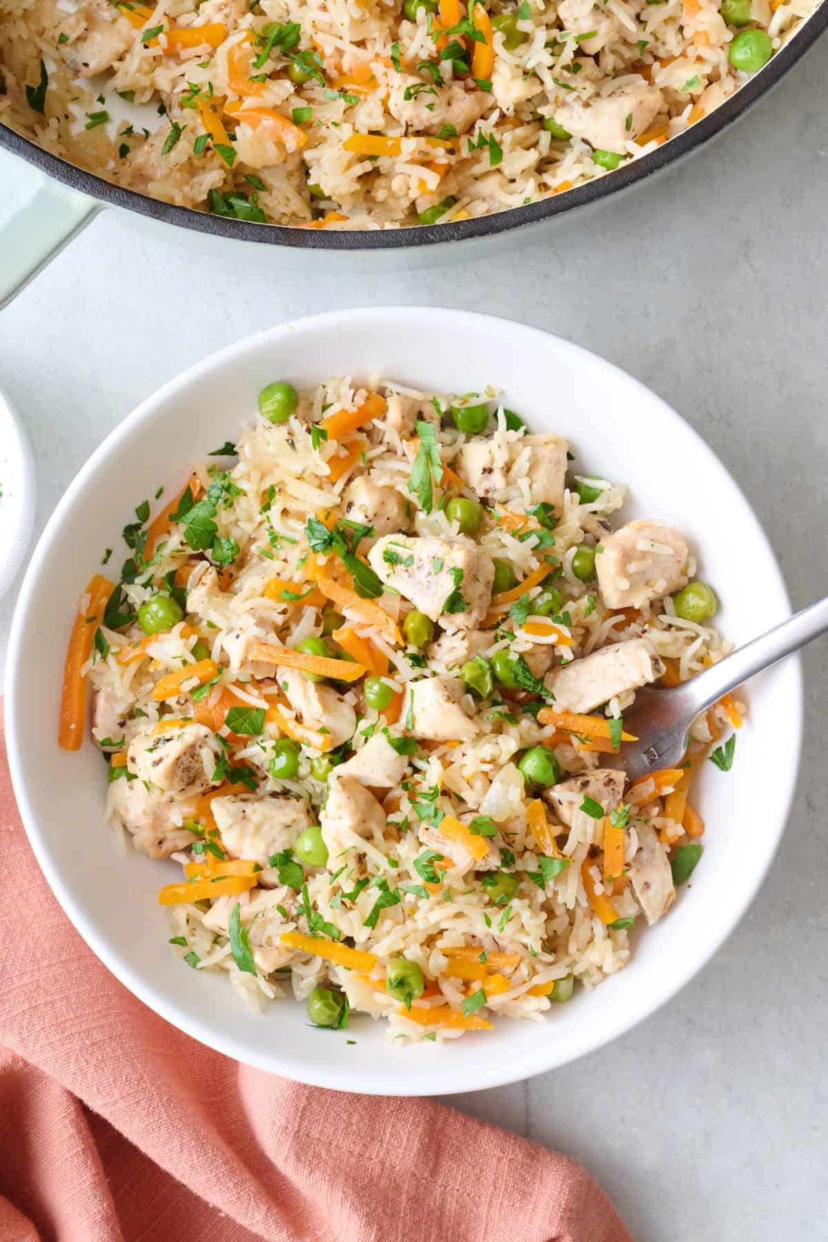 Bowl of one pot chicken and rice with peas, carrots, and parsley served with a fork.