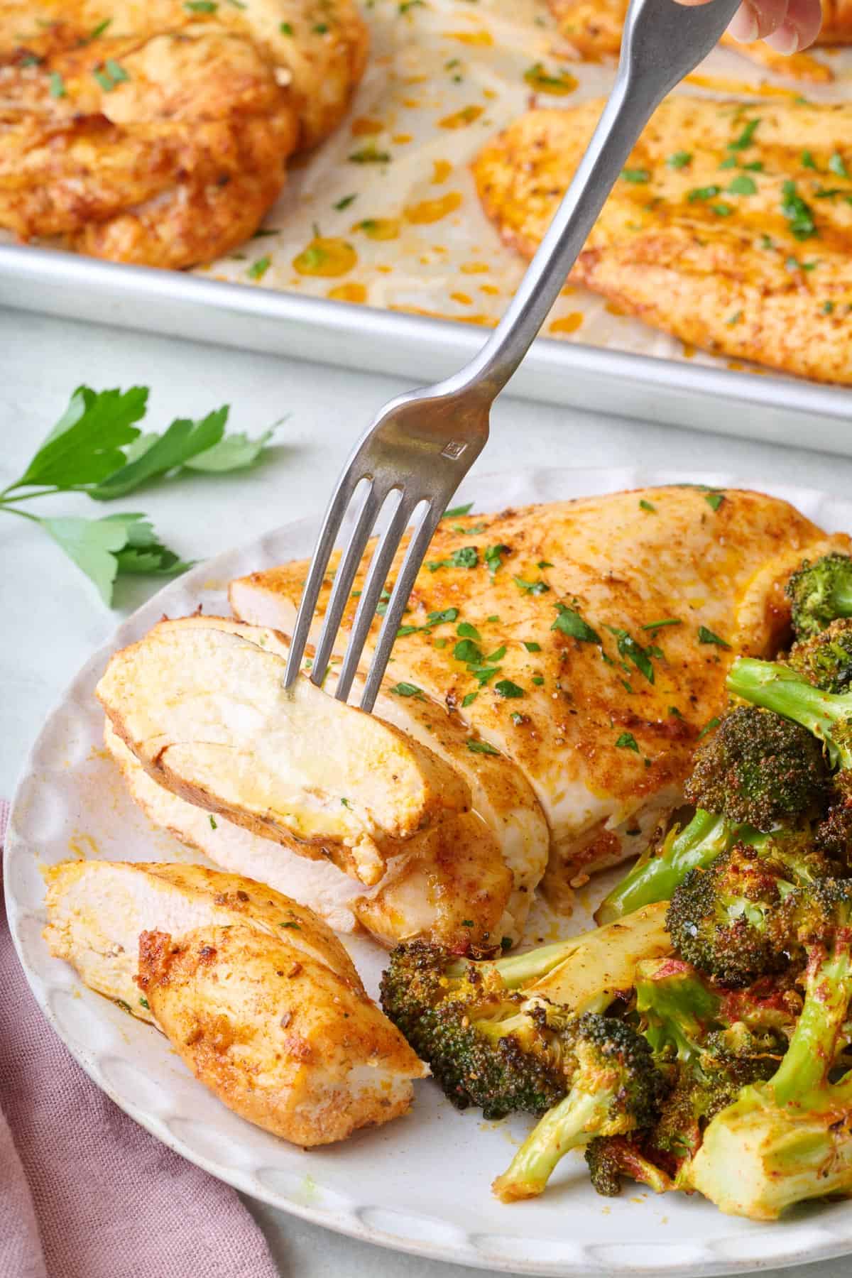 Fork lifting up a piece of baked chicken from a plate.