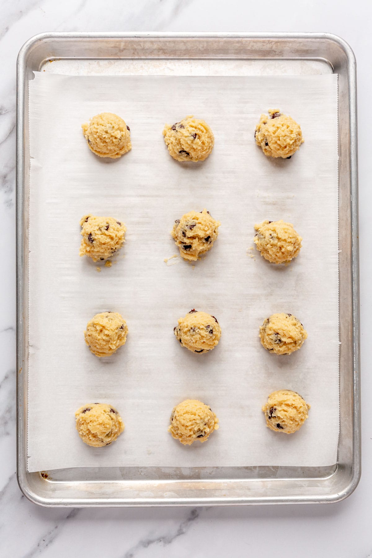 Cookie dough balls on a parchment line baking sheet.
