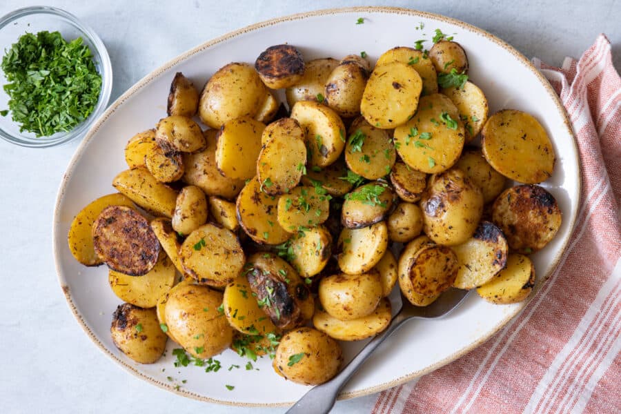 Platter with grilled potatoes garnished with parsley and spoon on side.