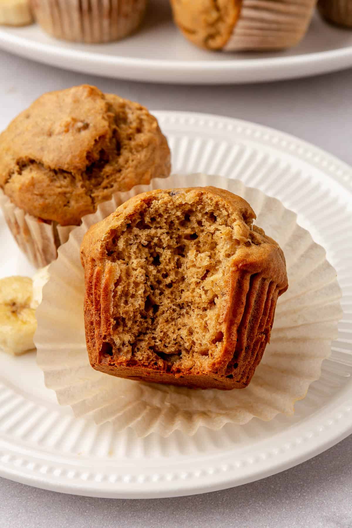 Peanut butter banana muffin on a plate with paper peeled back and a bite taken out to show texture.