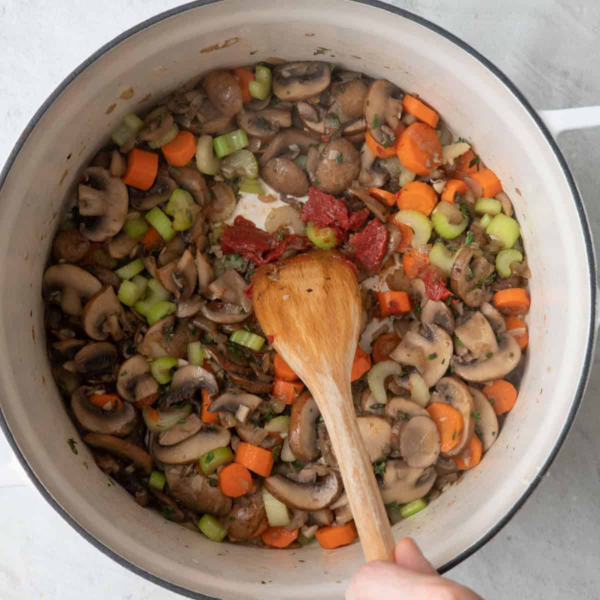 Tomato paste added and wooden spoon stirring it into veggies.