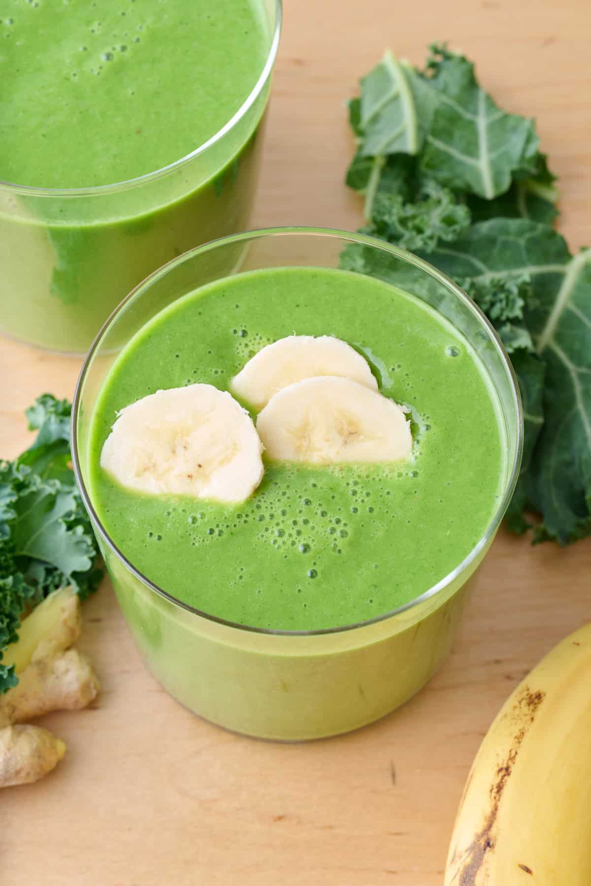 Bright green kale detox smoothie in two glasses, one topped with banana slices.