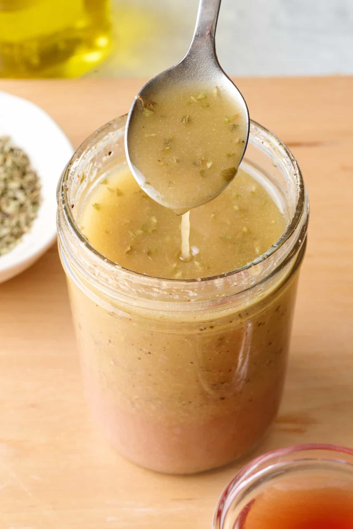 Homemade Greek salad dressing in a small mason jar with spoon lifting some up.
