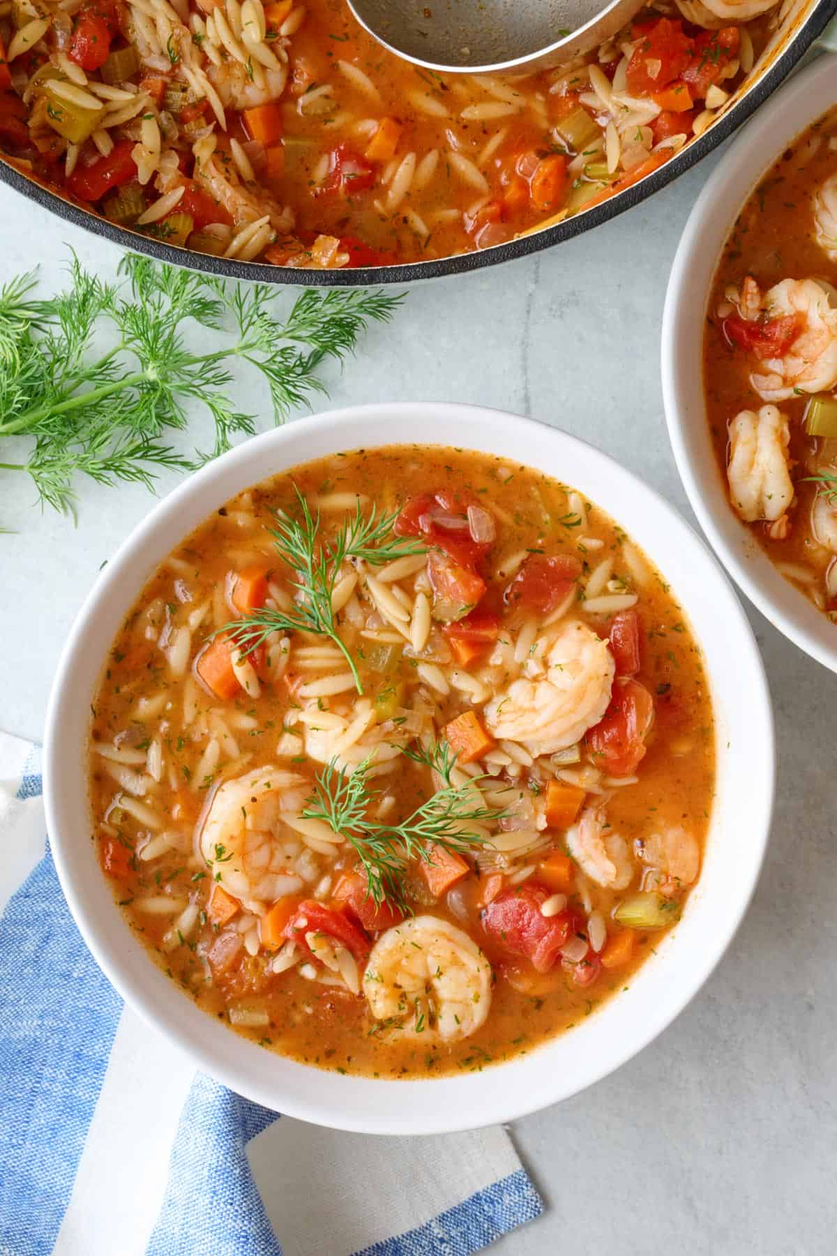 Easy shrimp orzo soup in a bowl with pot nearby.