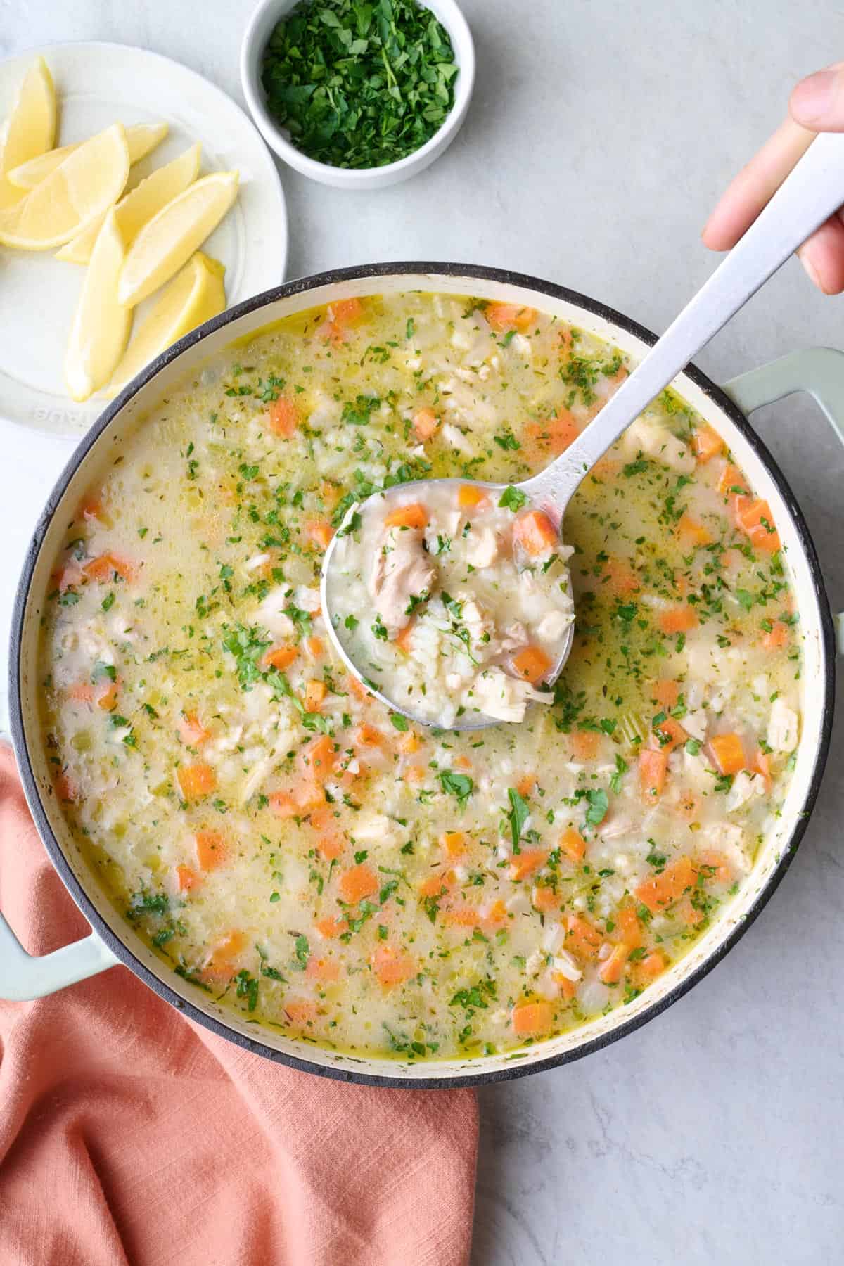 Chicken lemon rice soup in pot with ladle dipped inside and lifting some out.