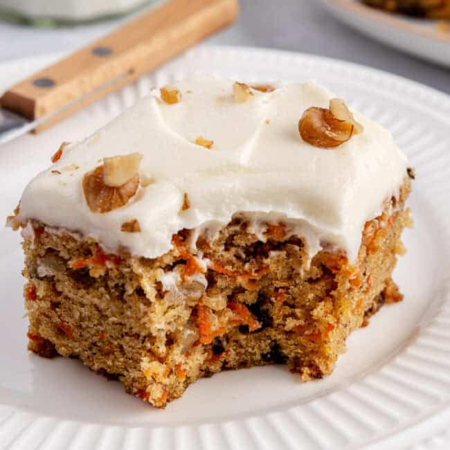 Slice of carrot cake on a plate with a bite removed.