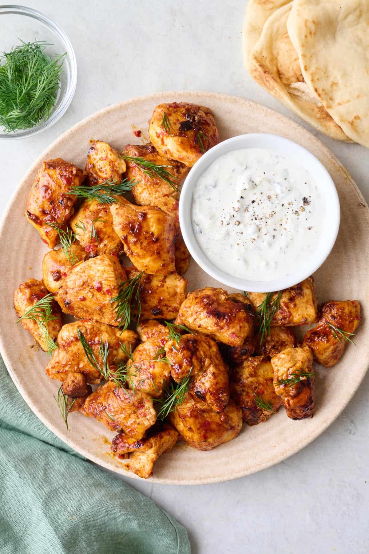 Spicy harissa chicken bites on a plate garnished with dill, small dish of yogurt sauce inside the serving bowl.