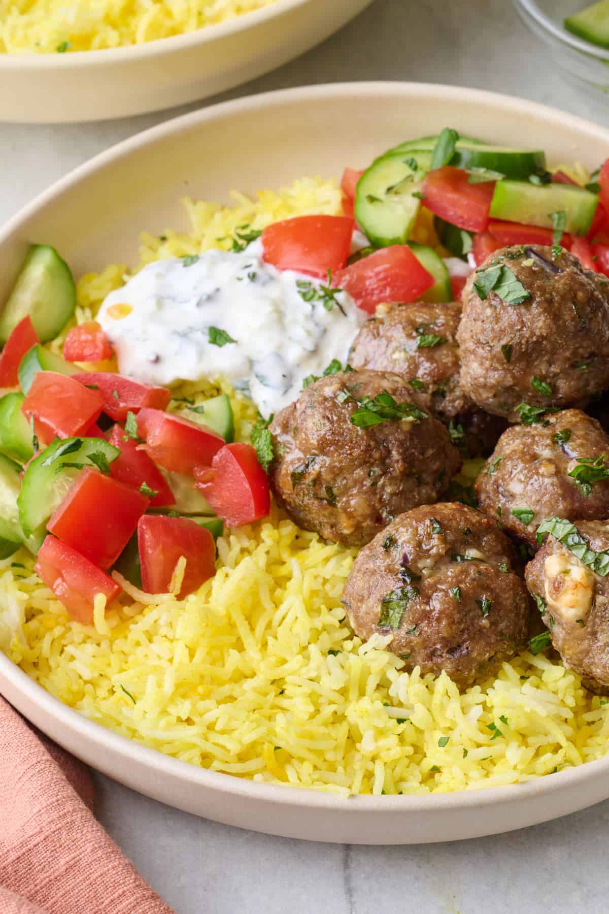 Bowl of lemon rice with lamb meatballs, chopped fresh cucumbers and tomatoes, and greek yogurt sauce on top.