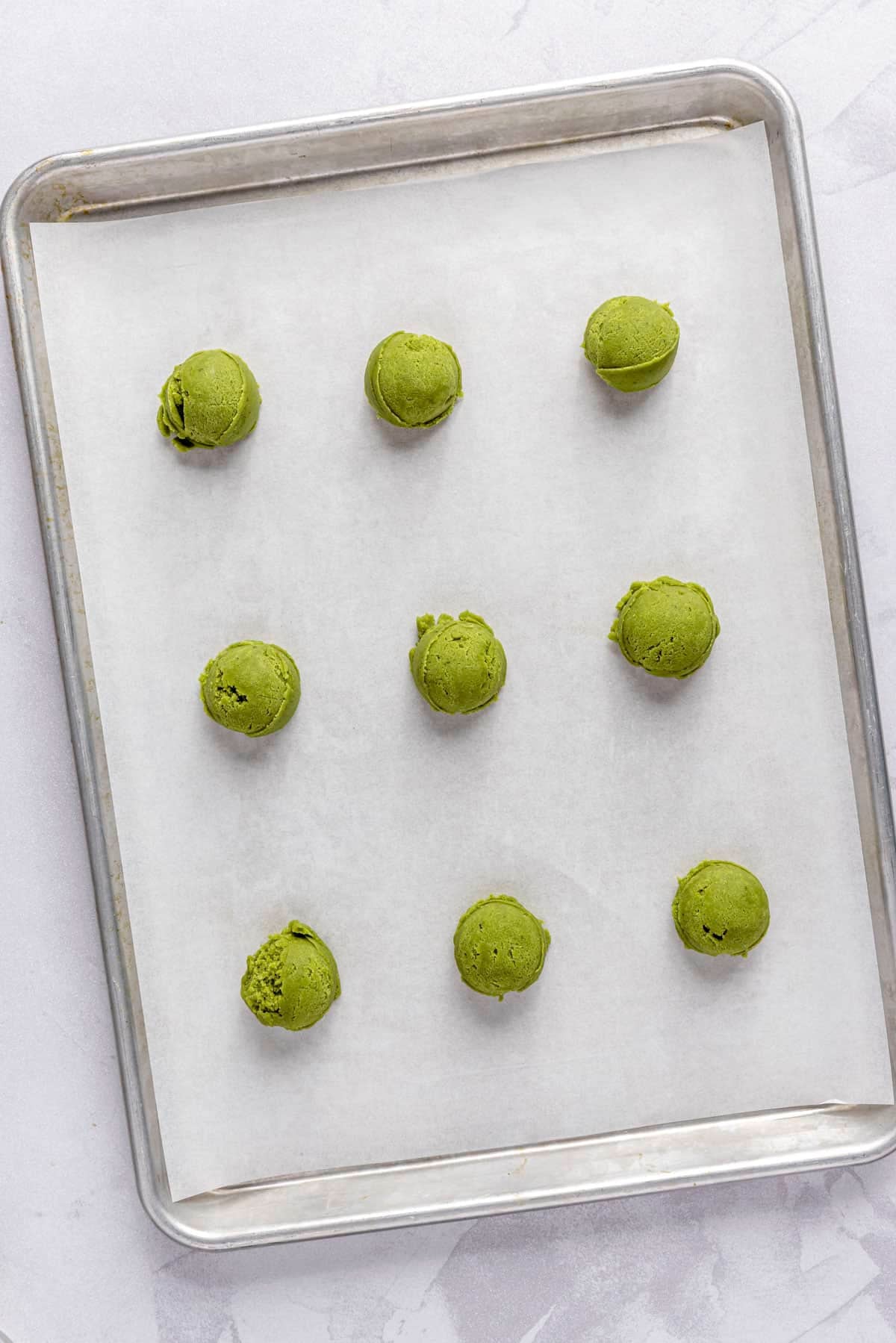 Cookie dough balls on a parchment lined sheet pan before baking.
