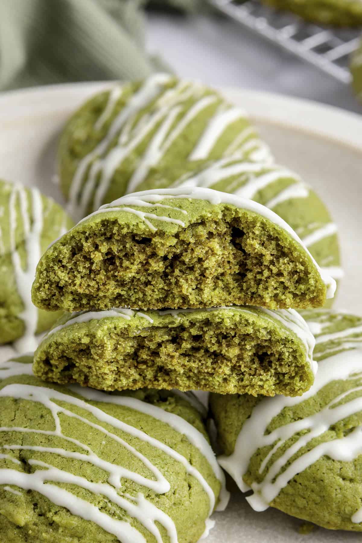 A matcha cookie split in half to show green inside texture, resting on a plate of more cookies.