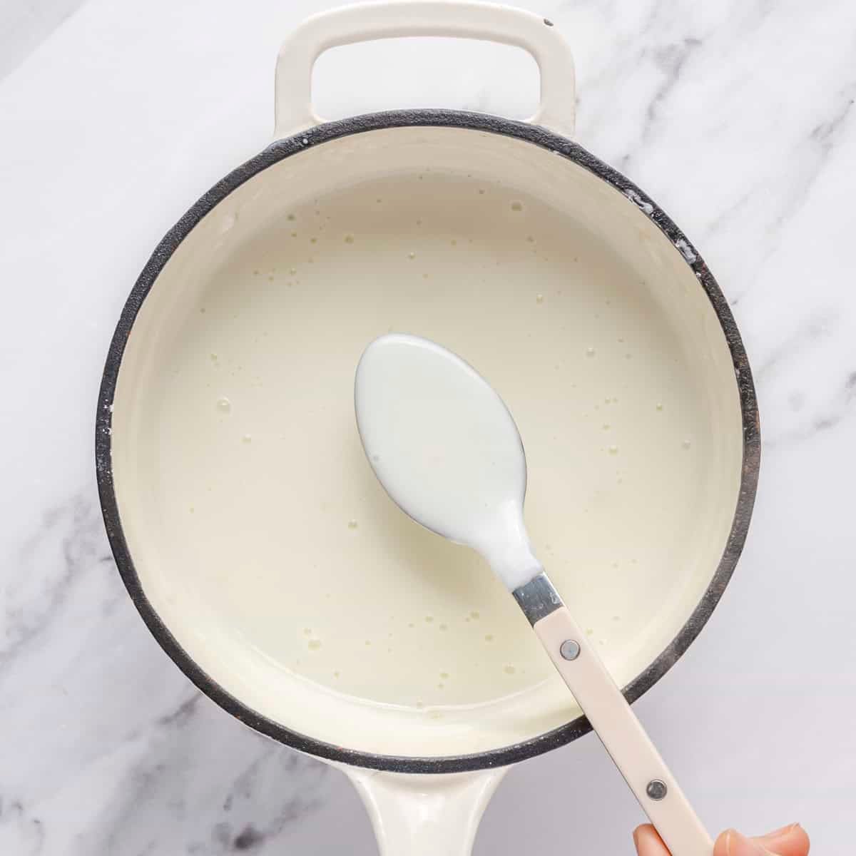 Spoon lifting up recipe from pot to show thickened consistency.