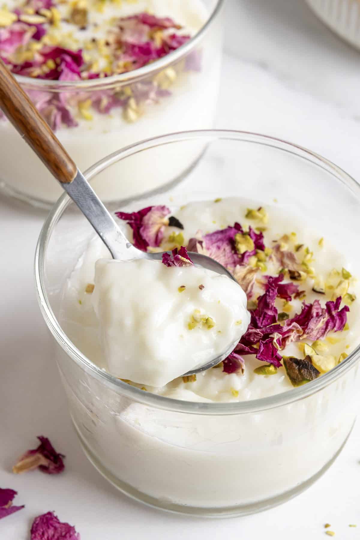 Spoon lifting up a bite of muhallabia from glass to show thick and creamy consistency.