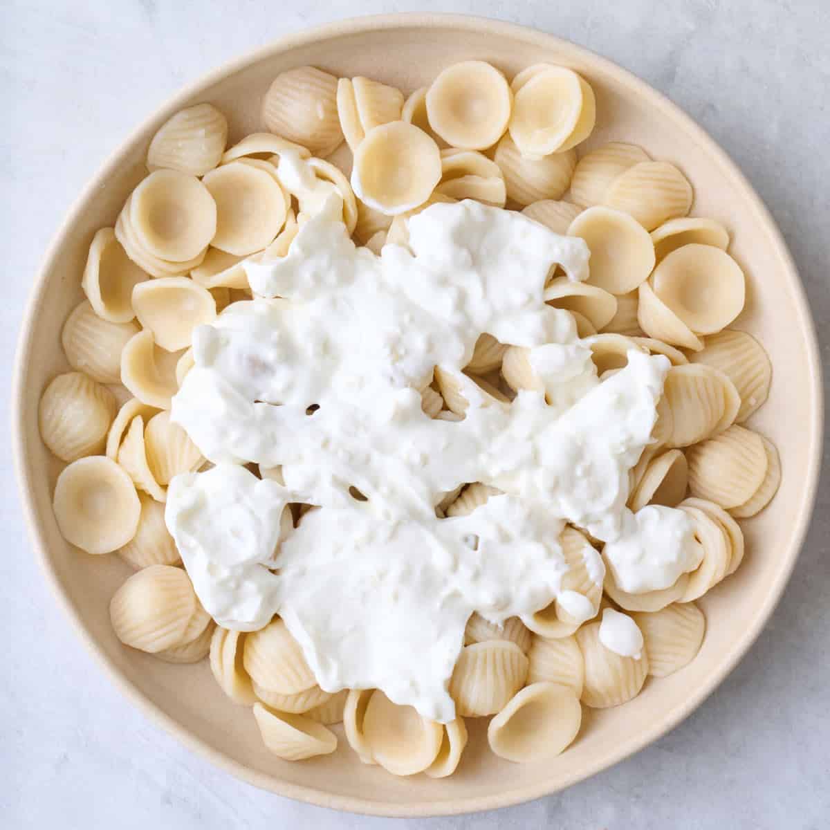 Yogurt sauce added on top of cooked pasta in a bowl.
