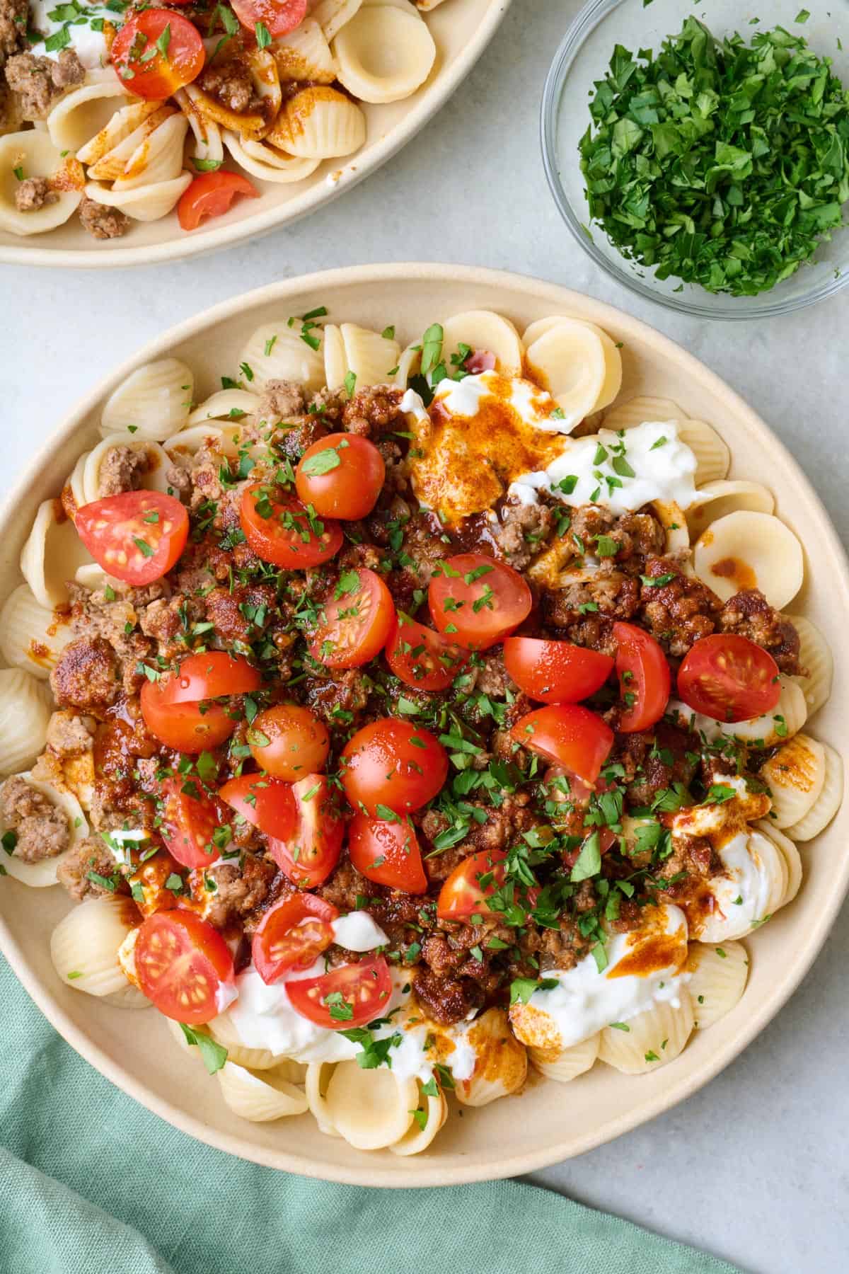 Bowl of Turkish pasta with seasoned ground beef, fresh tomatoes, paprika butter sauce, and yogurt sauce.