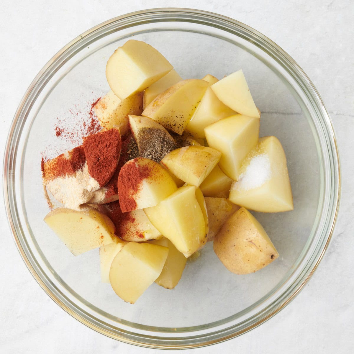 Potatoes, oil and seasonings in a bowl.