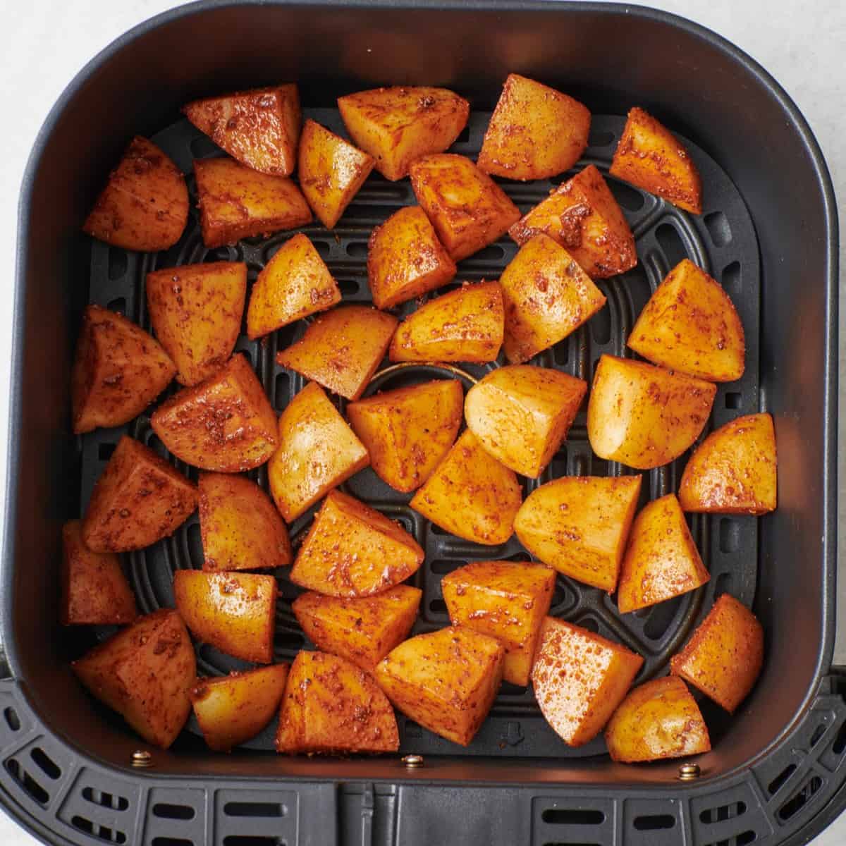 Seasoned potatoes in an air fryer basket.