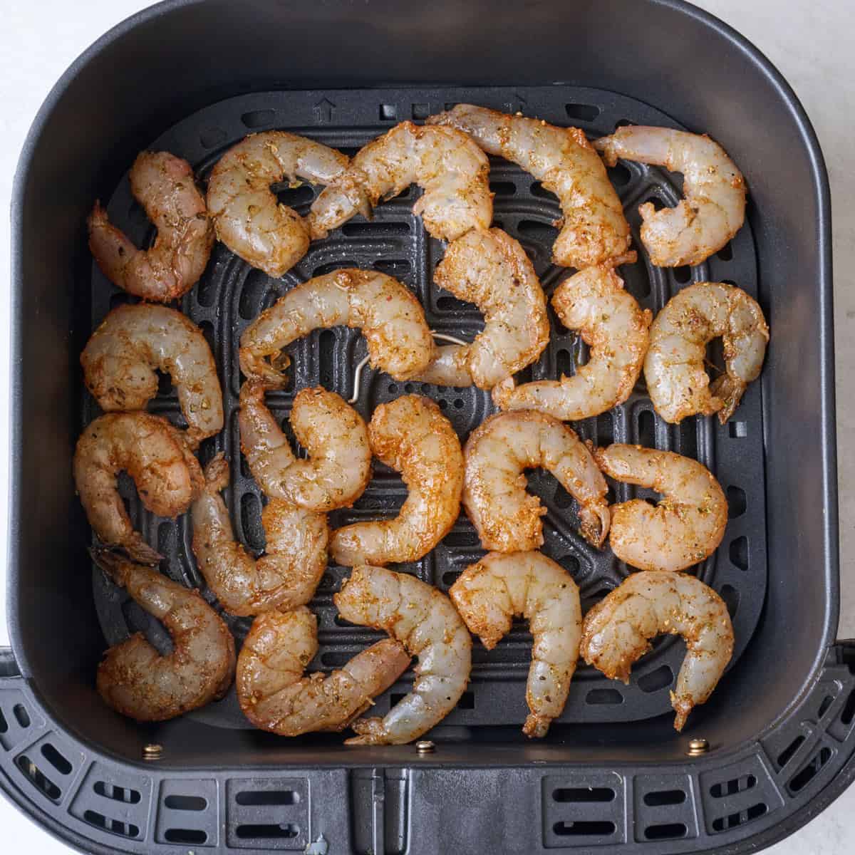 Shrimp in a single layer in air fryer basket.