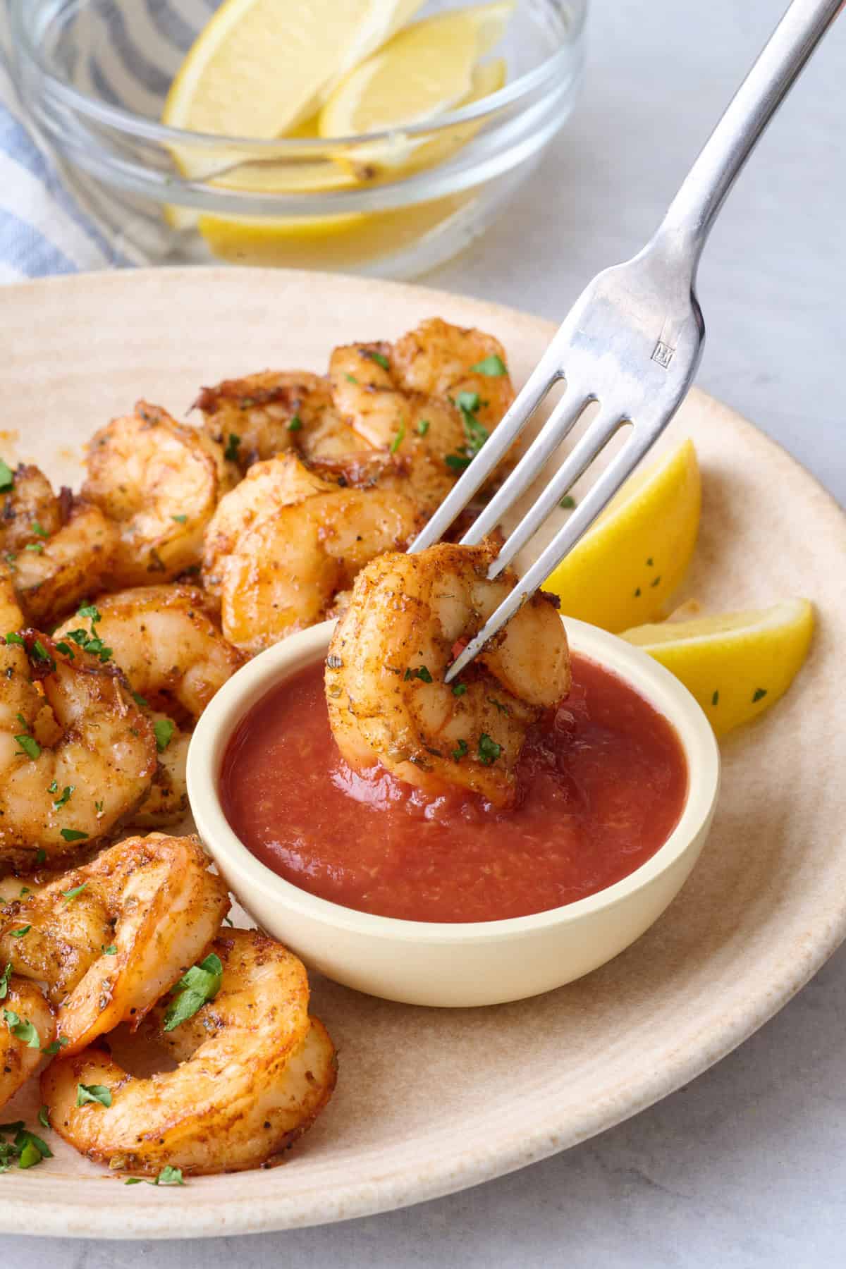 Air fried shrimp on a plate with a fork dipping one into cocktail sauce.