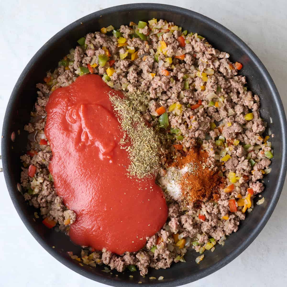 Tomato sauce and seasonings added to cooked beef and veggies in skillet.