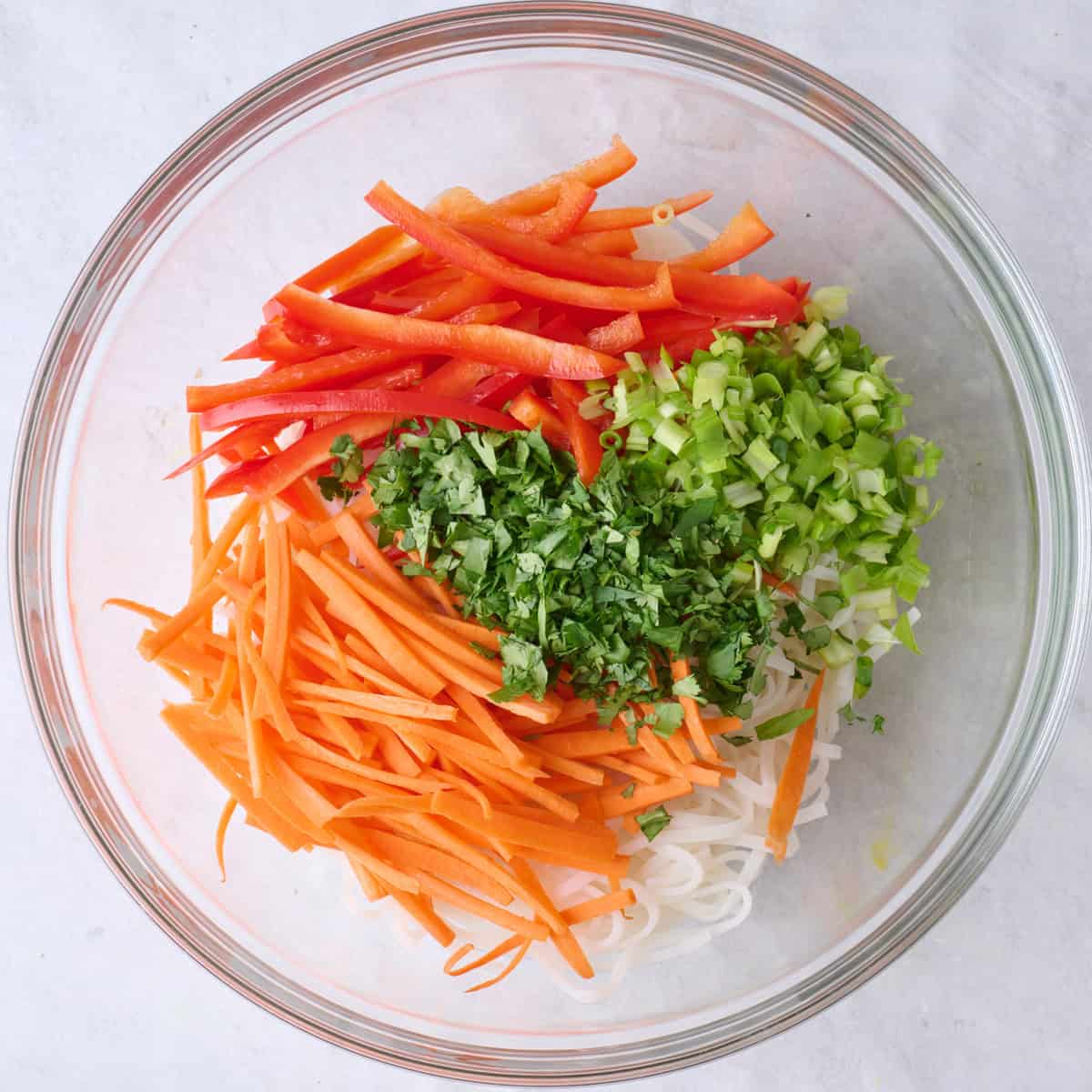 Sliced red peppers, carrots, cilantro, and green onions added to cooked rice noodles.