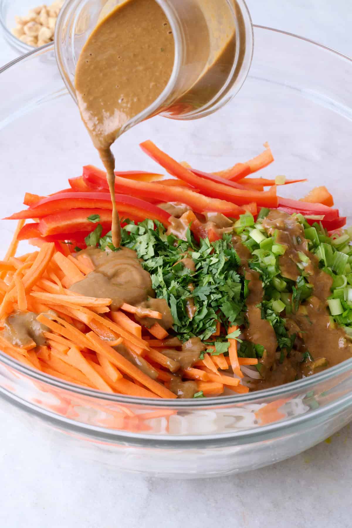 Pouring dressing over untossed noodles and veggies in bowl.