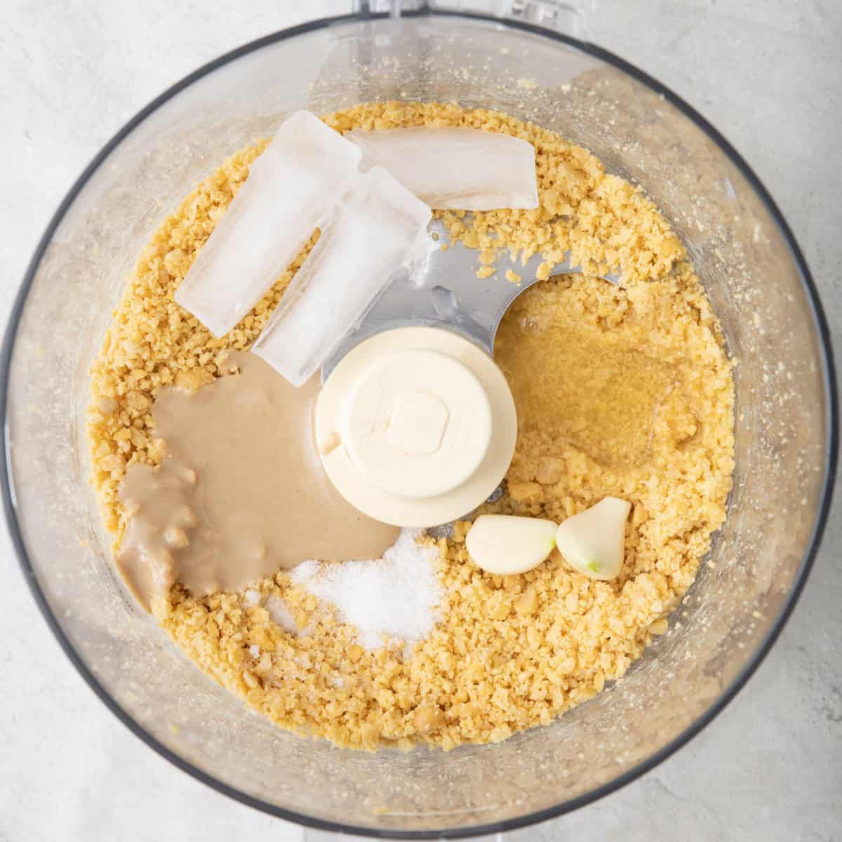 Ice cubes, tahini, salt, and garlic added to processed chickpeas.