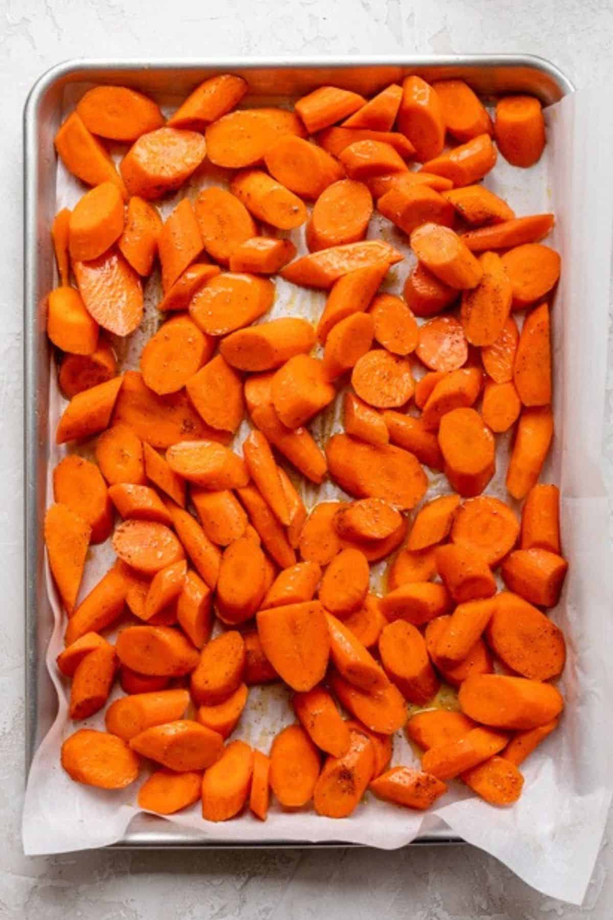 Carrots cut and tossed in oil and spices on a sheet pan.