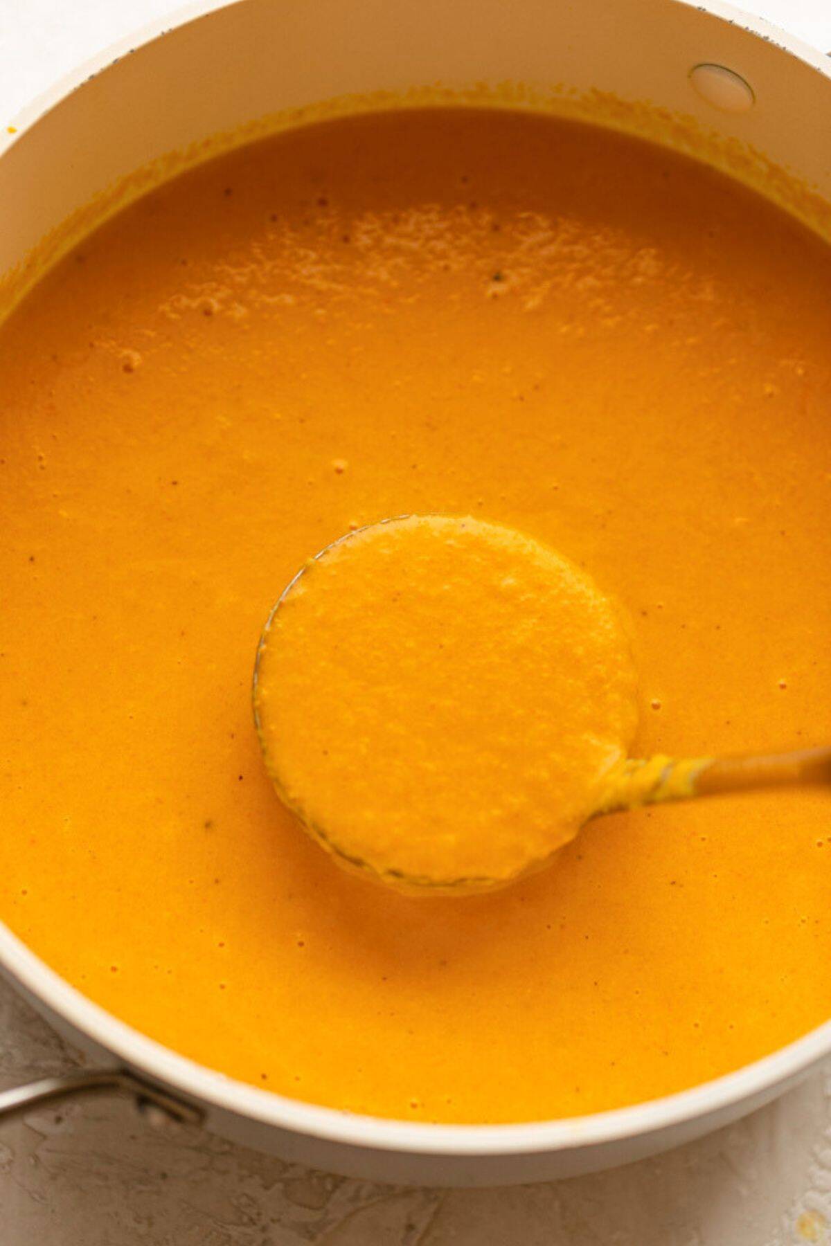 Ladle lifting up carrot ginger soup from pot.