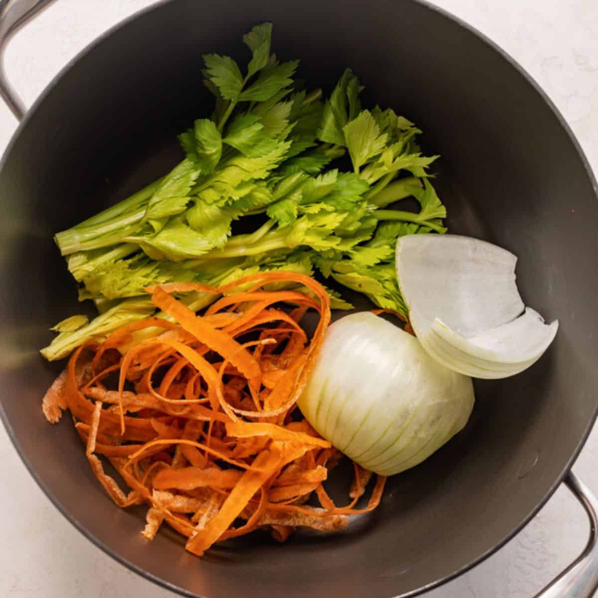 Onion and carrot skins and celery stalk tops in a pot.