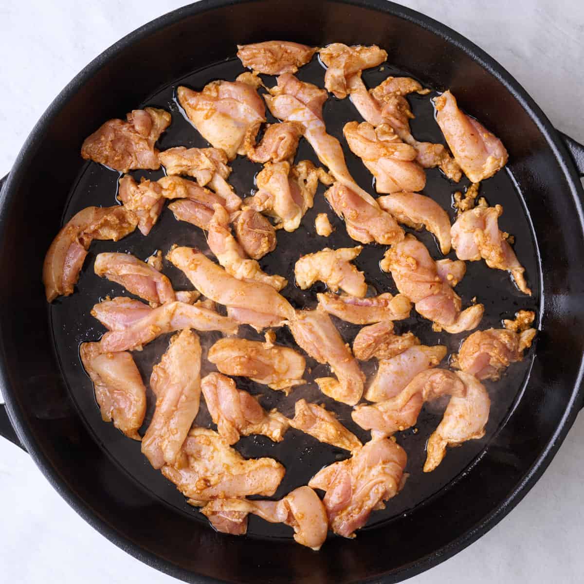 Seasoned chicken pieces in a hot oiled skillet.