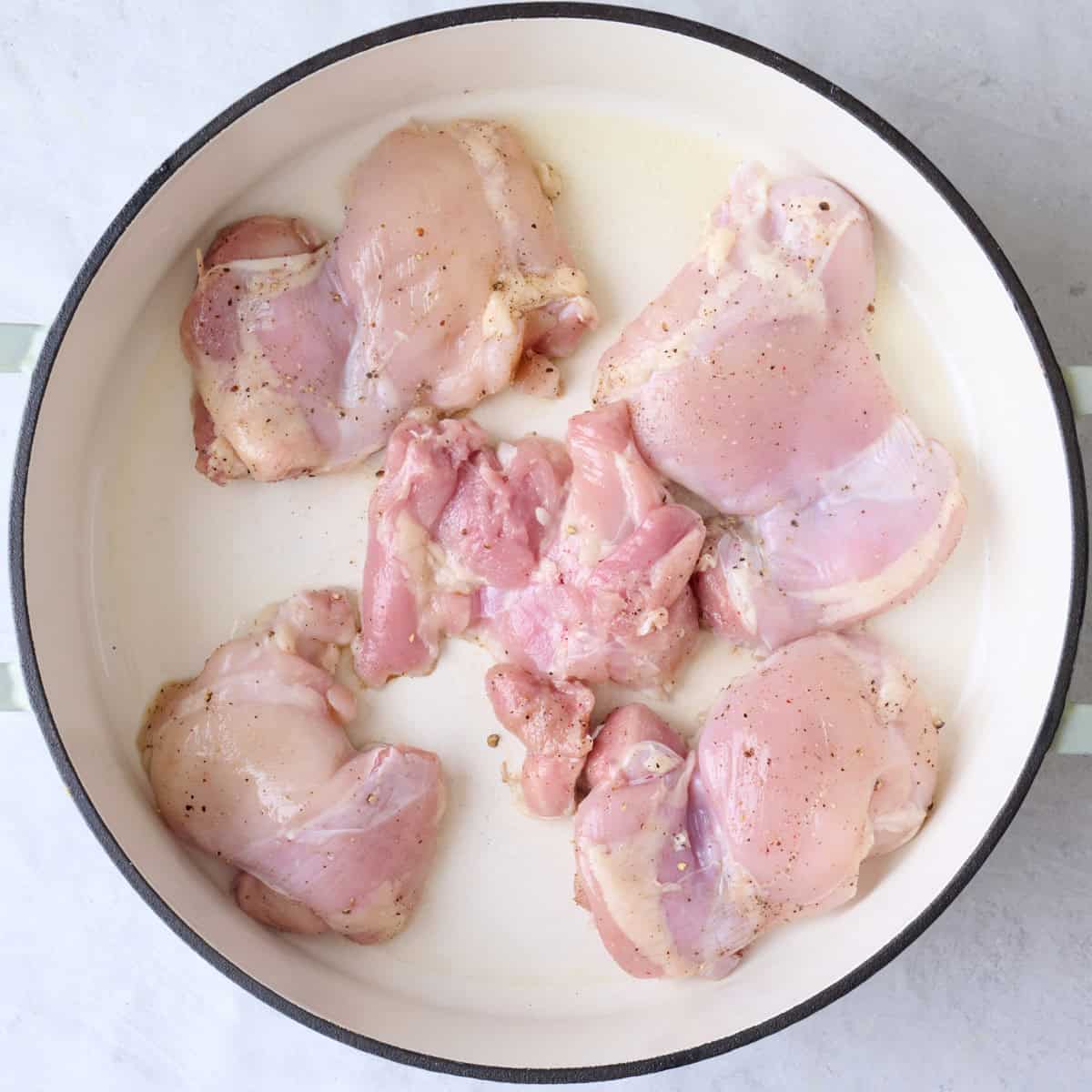 Seasoned thighs in oiled pot.