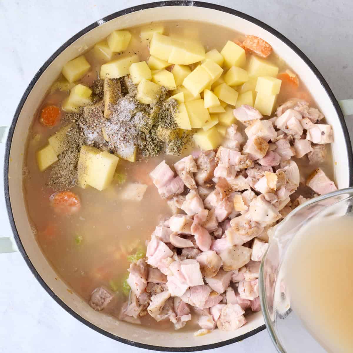 Diced cooked chicken thighs, broth, potatoes, rosemary, thyme, sage, and remaining salt and pepper added before stirring.