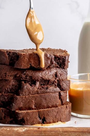 Stack of sliced chocolate peanut butter banana bread with a spoon drizzling it with peanut butter.