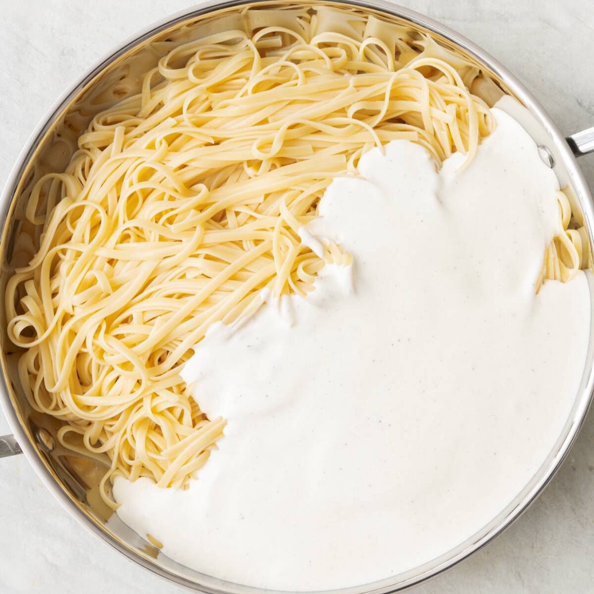 Cottage cheese sauce added to cook pasta in skillet.