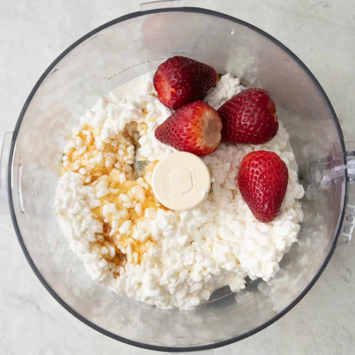 Cottage cheese, honey, and fresh strawberries in a food processor before blending.