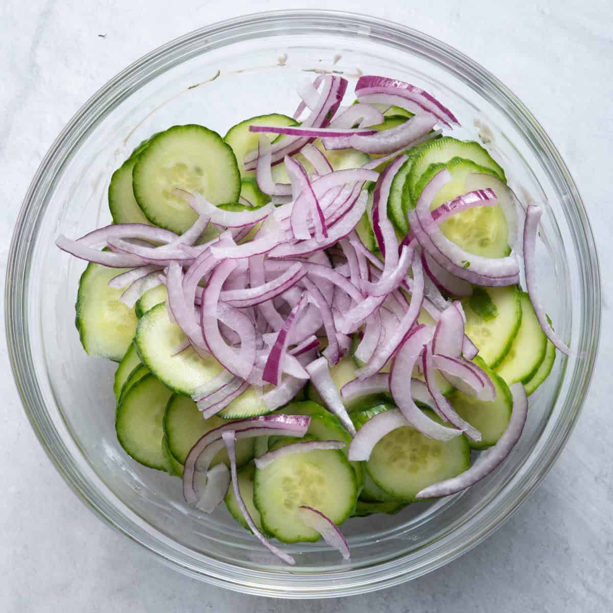 Cucumber slices and sliced red onion on top of dressing.