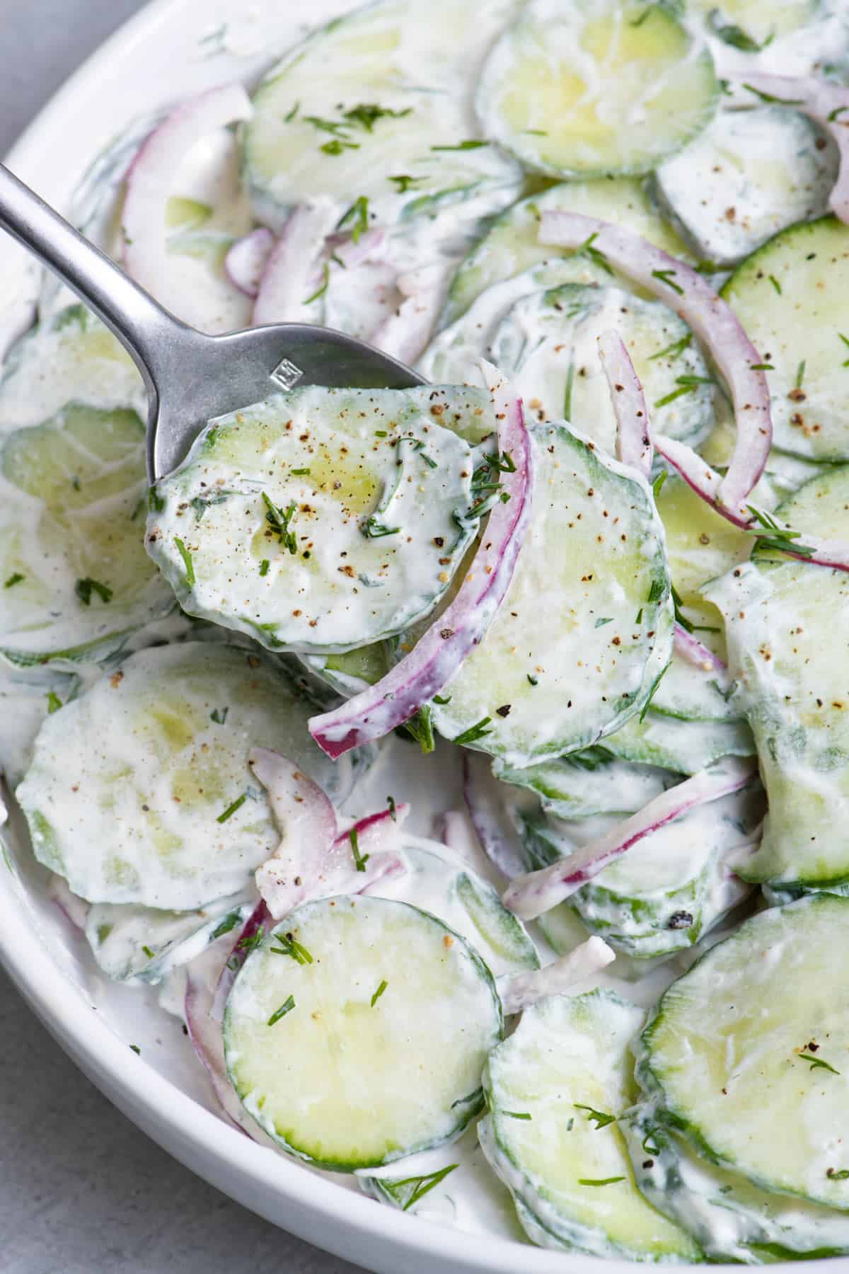 Spoon lifting up a bite of creamy cucumber salad with red onions.