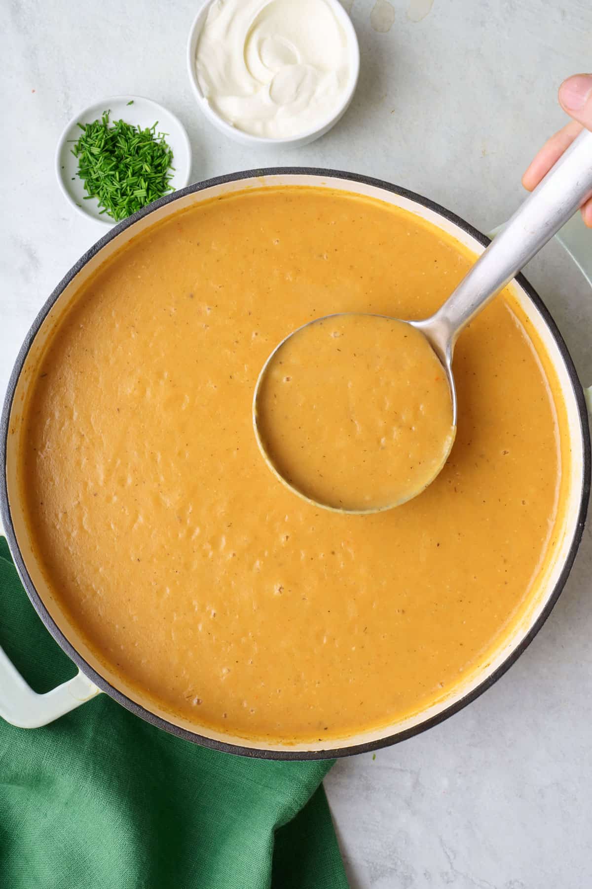 Creamy potato soup in a pot with a ladle lifting some up.