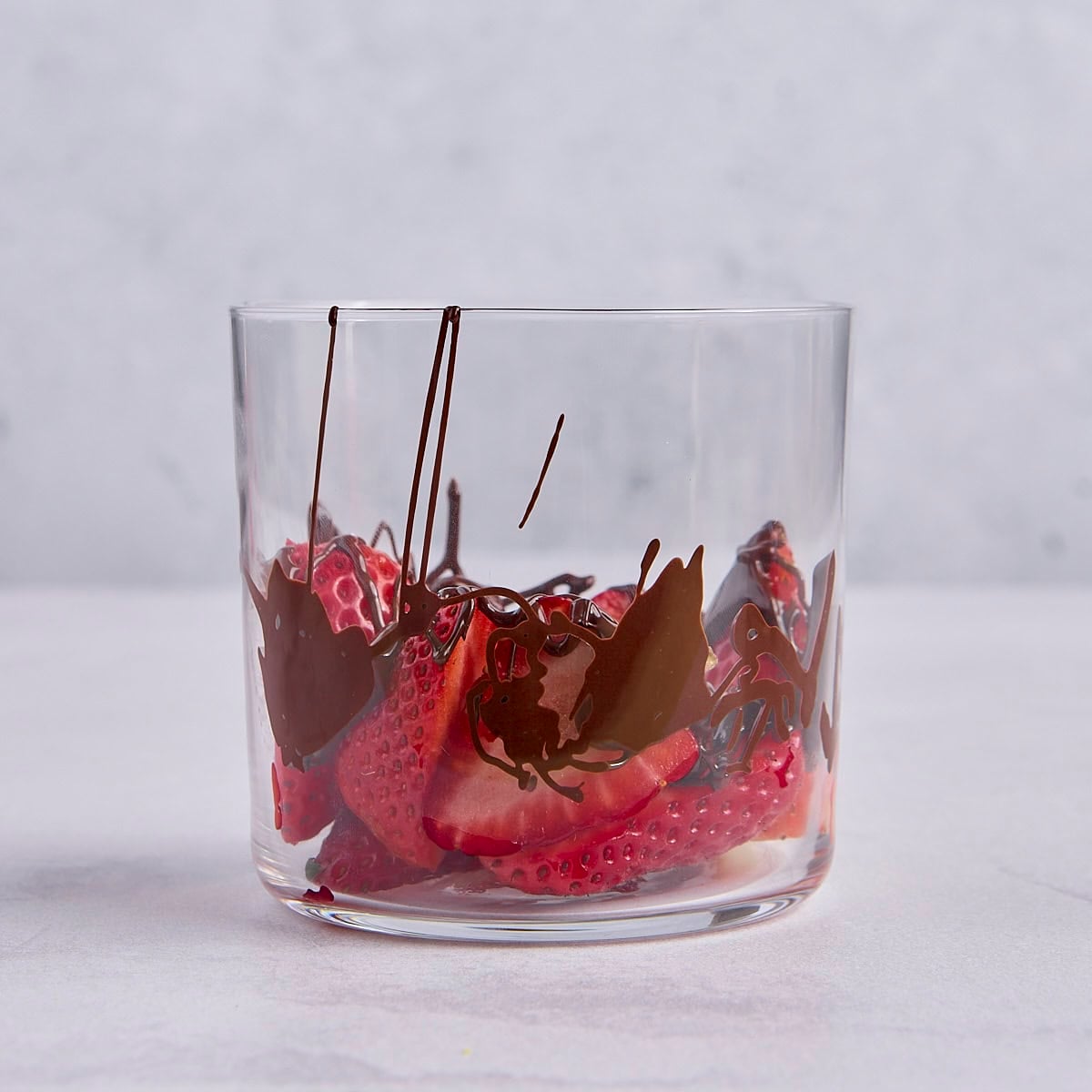 Sliced strawberries in a small dessert cup with melted chocolate drizzled on top.