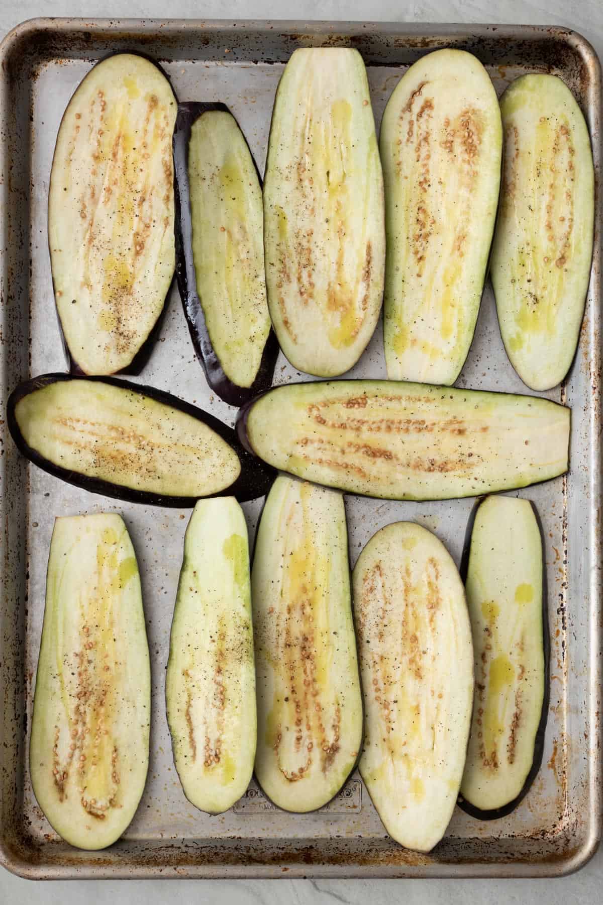 Eggplant slices after patting dry coated with oil and pepper on a sheet pan.