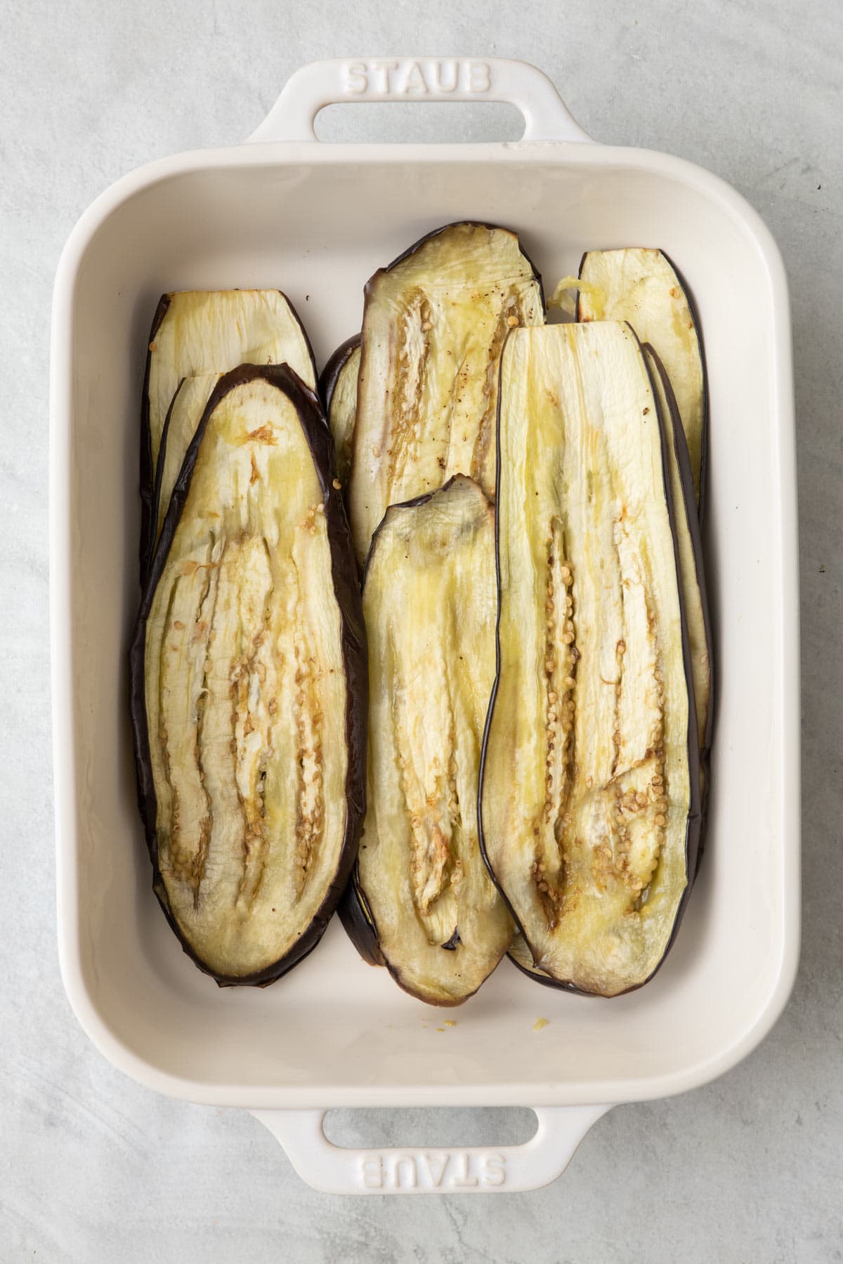 Cooked eggplant slices arranged in baking dish.