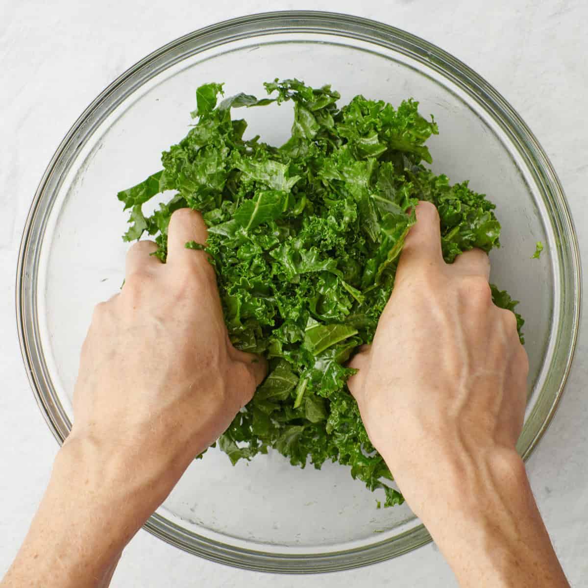 Hands massaging kale and dressing together.