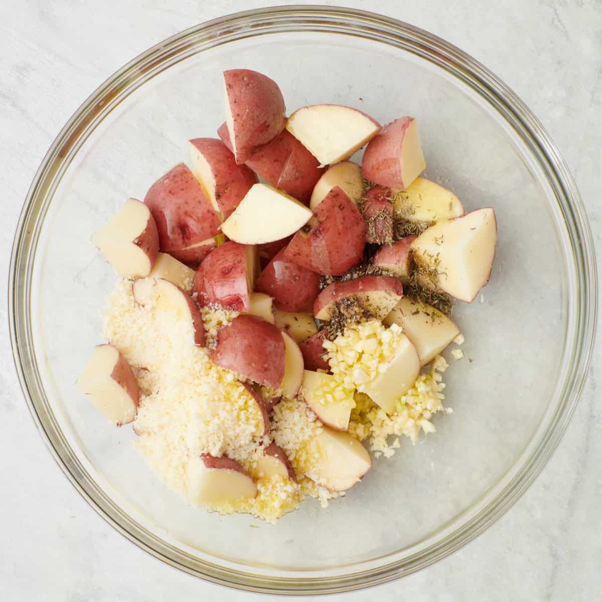 Diced potatoes in a bowl with oil, garlic, parmesan, dried thyme, salt and pepper.