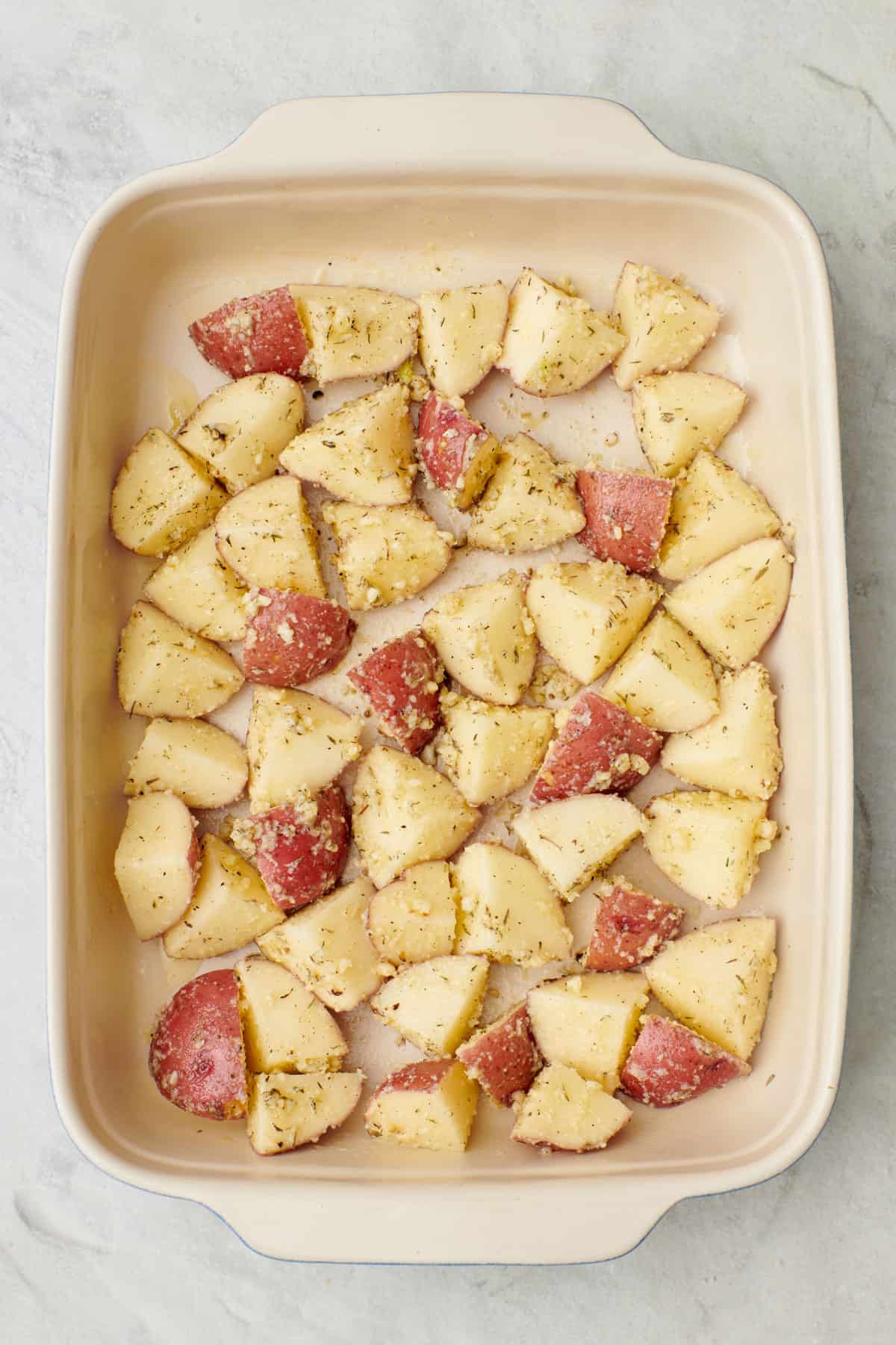 Seasoned potatoes in a baking dish before roasting.