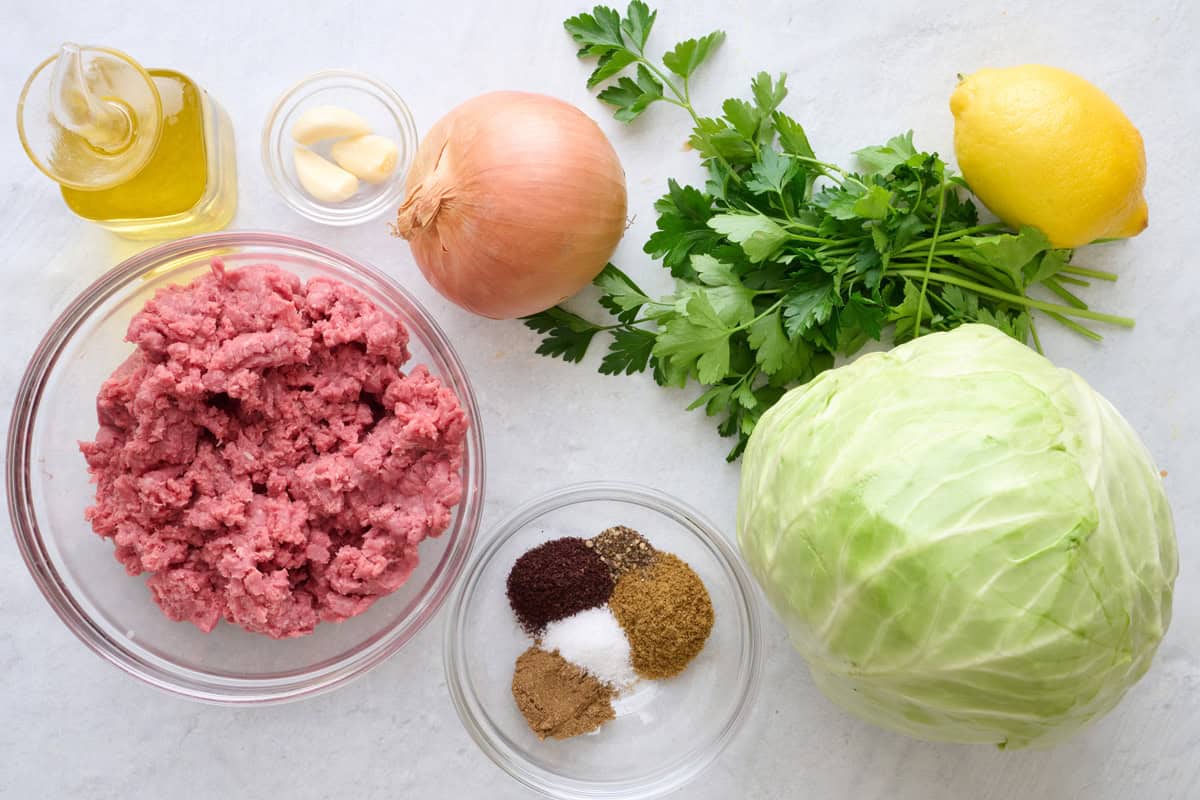 Ingredients for recipe before prepping: oil, garlic, ground beef, onion, spices, fresh parsley, cabbage, and lemon.