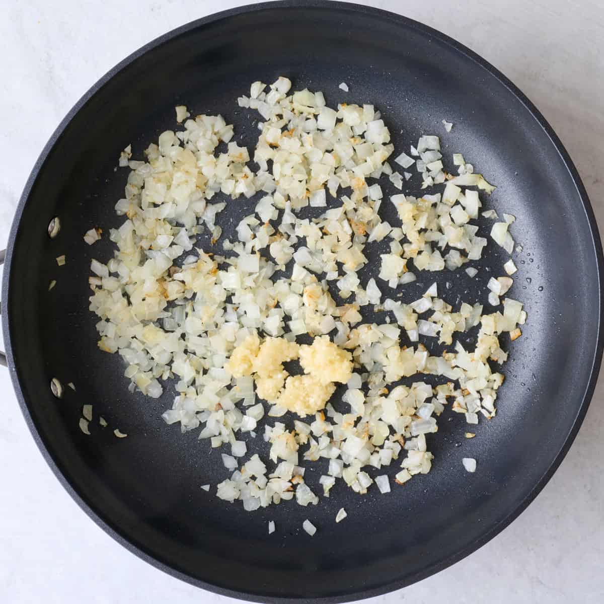 Onions in an oiled skillet after cooking with minced garlic added.
