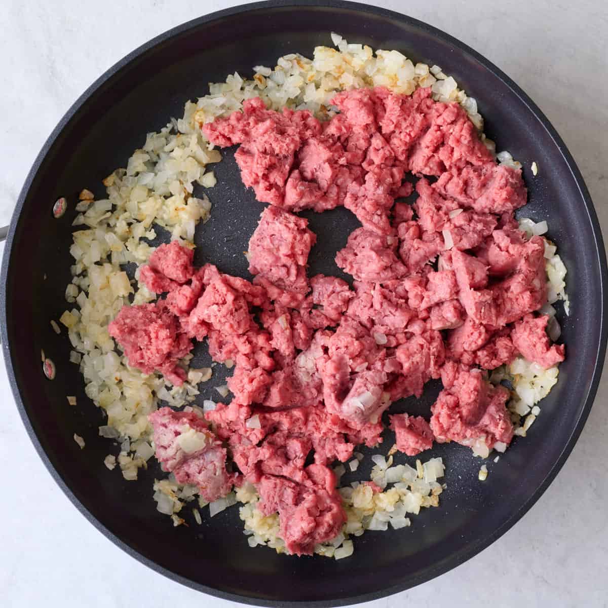 Ground beef added to cooked onions in pan.