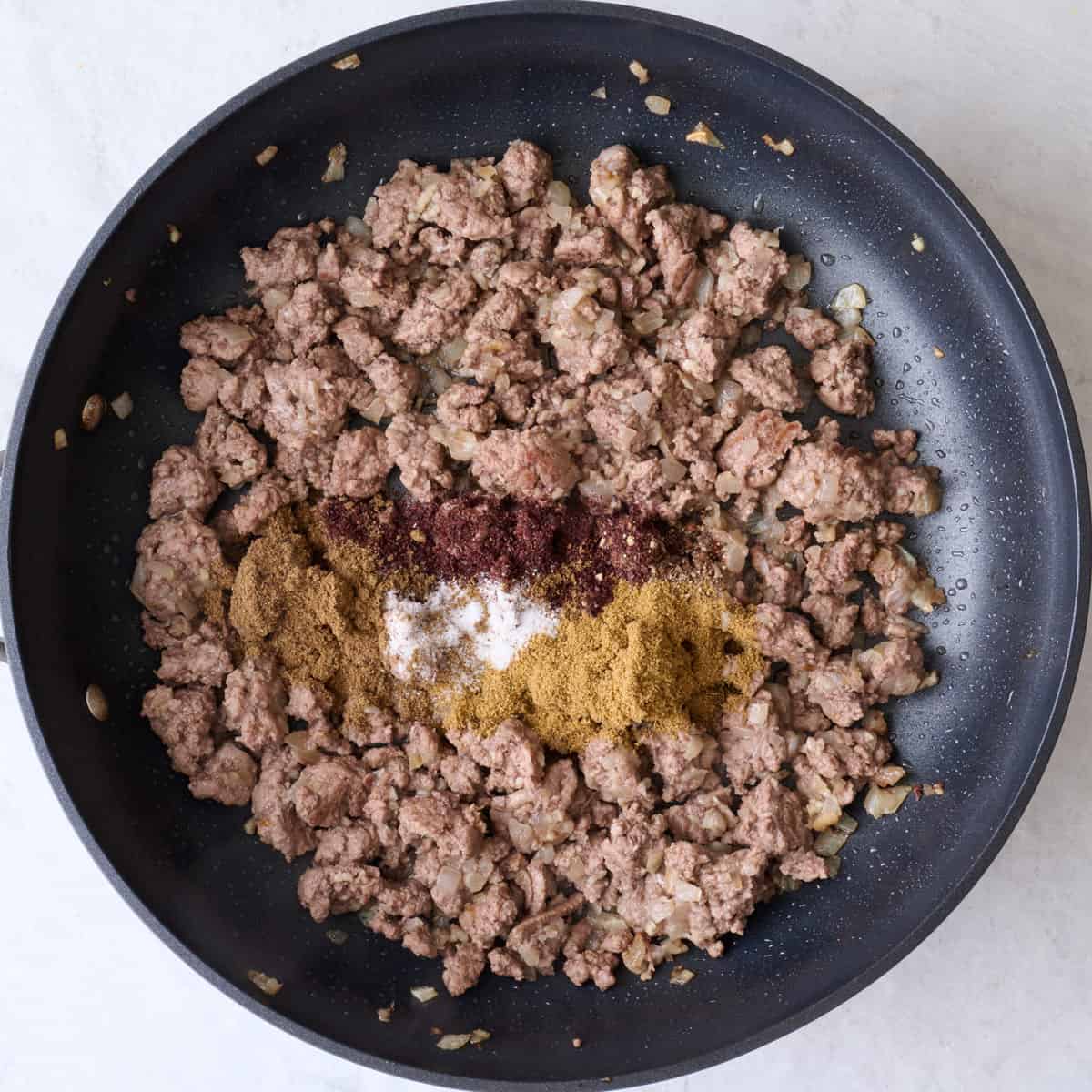 Cooked ground beef in a pan with spices added.