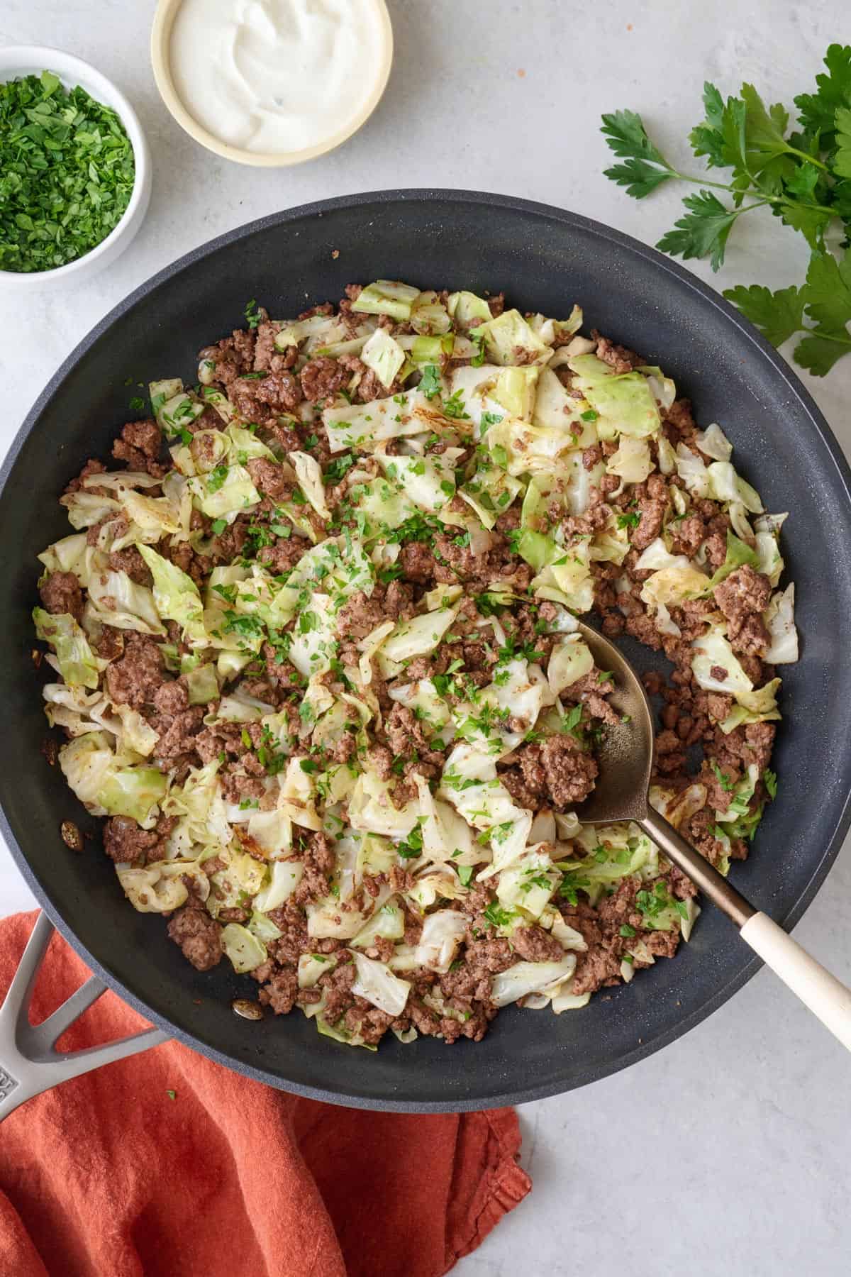round beef and cabbage in skillet garnished with fresh parsley, and a small dish of yogurt nearby.